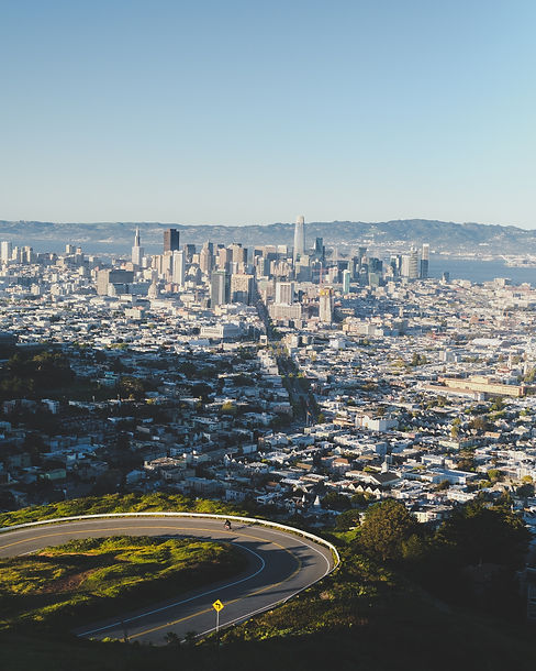 vertical-shot-curvy-road-down-hill-with-city-buildings-distance-blue-sky.jpg
