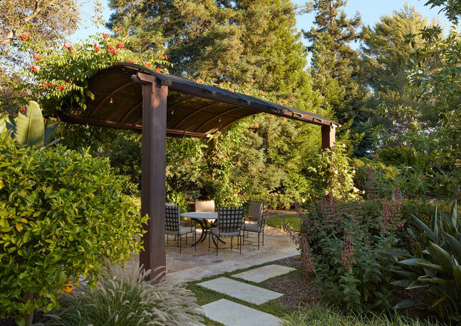 Shaded outdoor dining area under a metal pergola with a flagstone path.