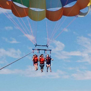 Three people parasailing under a colorful parachute.