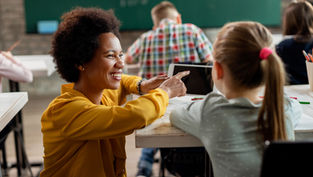 Smiling teacher guiding a young student with a digital tablet in the classroom, representing LAPU’s education programs that prepare future educators to inspire the next generation.