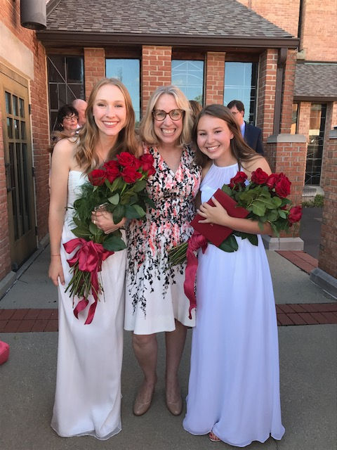 A parent takes a photograph of Ms. Fischer with two of her seniors at graduation.