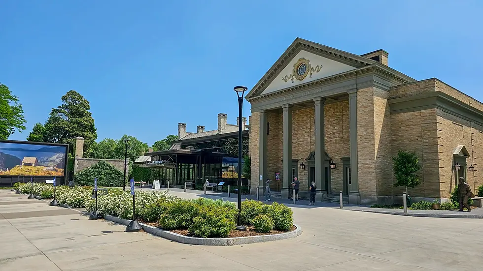 Sunny view of a brick museum building, the George Eastman, with columns, blue sky, visitors outside, and a large landscape sign.