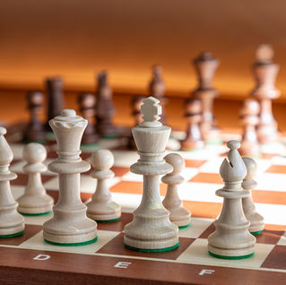Wooden chess pieces on a checkered board in warm sunlight, with letters C to G visible on the edge and a calm, focused mood