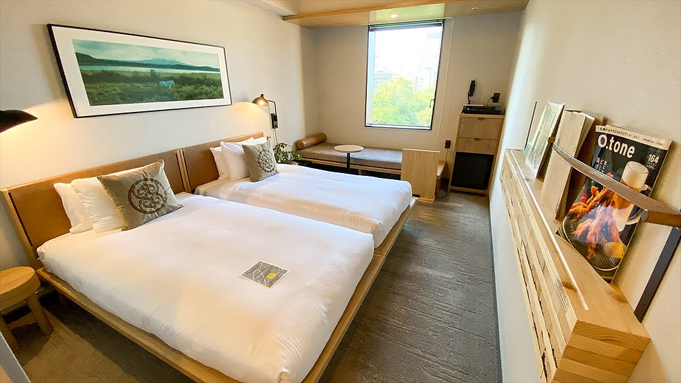 Modern hotel room at Royal Park Canvas Hotel Sapporo with two beds, wall art, and a window view. Magazines on a rack, and neutral tones create a calm atmosphere.