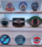 Car club badges from different regions displayed on shelves. Badges feature various designs, colors, and logos, with "Morgan" text visible.