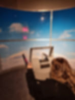 A person using a telescope in front of a sky simulation with clouds, part of a game at Silverstone museum. A digital display shows "Score 0022" and "Accuracy 66".