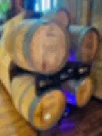 Wooden barrels labeled "Samuel Adams" and "Madeira" stacked on metal racks in a rustic setting with a wooden floor and ambient lighting at the Samuel Adams Boston Brewery tour.