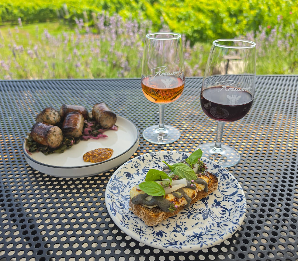 Two wine glasses and gourmet appetizers on a patio table, with a sunny garden blurred behind at Rosewood Winery.
