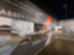 Racing-themed wall graphics at Silverstone Museum with images of cars on track, labeled corners like Abbey Curve and Farm Curve. Red, gray, black tones. Text quotes.