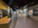 Silverstone Museum hallway with informative wall displays and a lit exhibit table. Walls feature historical photos and text. Dimly lit, modern design.