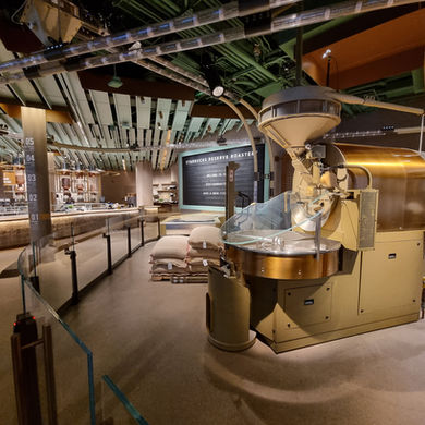 Starbucks Reserve Chicago roastery brand visitor experience interior with a large coffee roaster in the foreground, bags of beans, and a modern counter. Warm lighting and industrial decor.