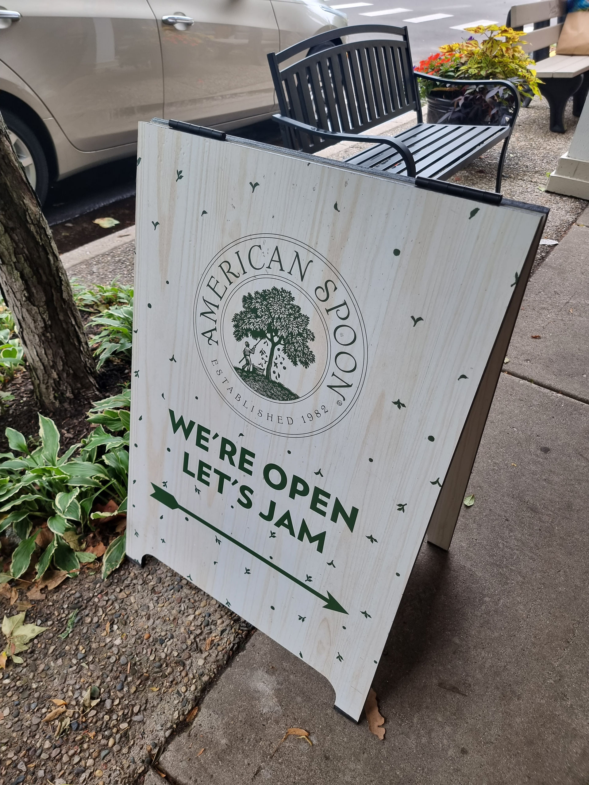 a wooden a frame sign stands on the sidewalk with text on it advertising american spoon