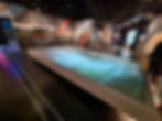 Exhibit room in the Silverstone museum with large digital floor map of a racetrack, walls featuring racing images and texts like "Copse Corner." Dimly lit setting.