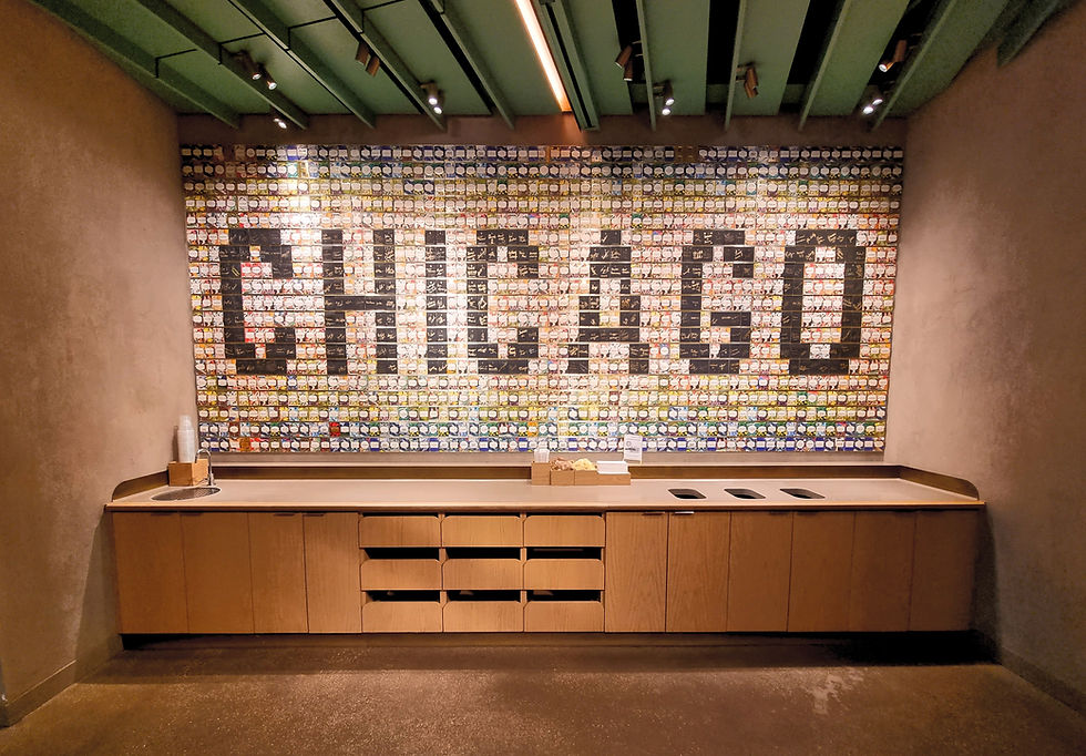 Wall features "CHICAGO" made of colorful tiles in a room with green ceiling and wooden cabinets. Three waste bins are on the counter.