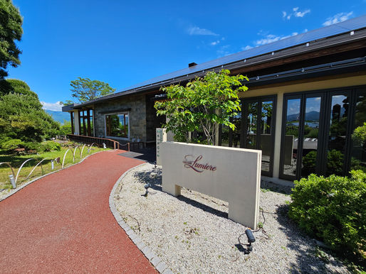 Luxury Lumiere winery visitor centre main building with solar panels and a Lumière sign beside a red path under a bright blue sky.