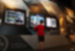 A child in a red sweater interacts with Silverstone museum exhibits on a Frazer Nash display. Comics and car-themed panels on walls. Text includes "The 500 Club was created in 1946."