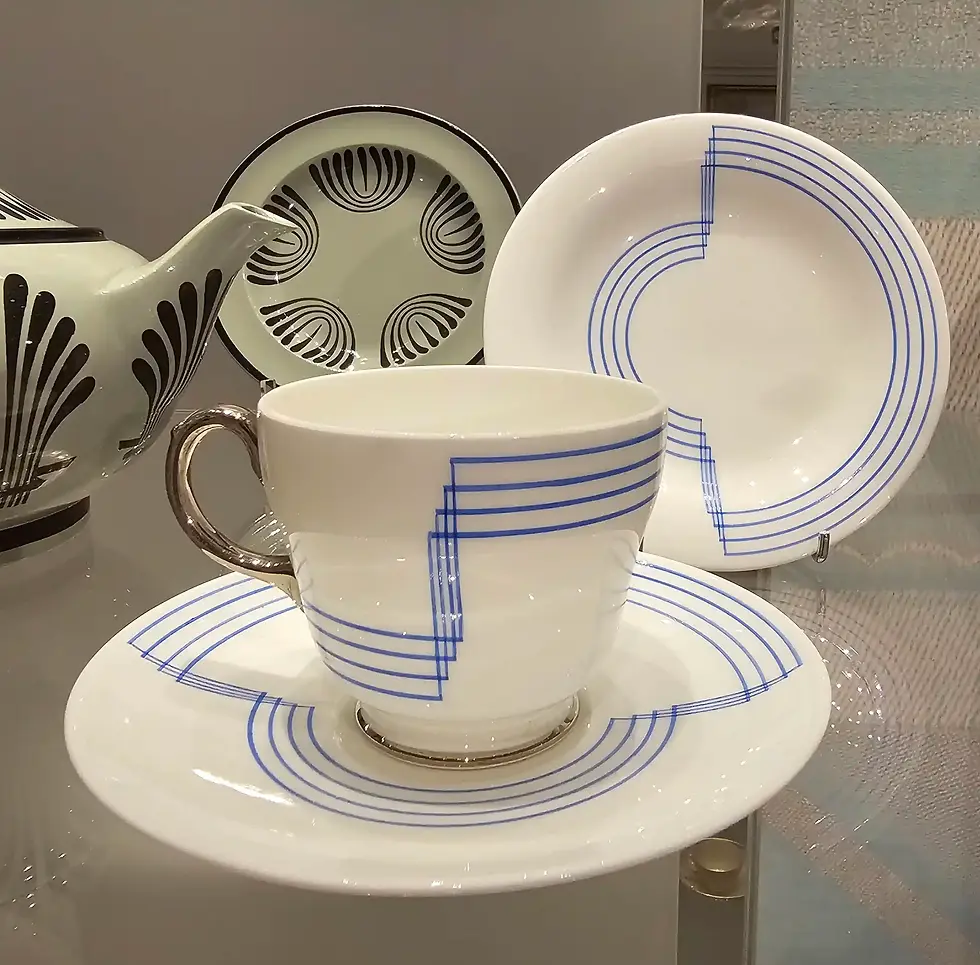 Art deco tea set with white and blue linear patterns, including a cup, saucer, plate, and teapot with black fan designs on a display at the World of Wedgwood V&A Museum.