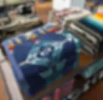 Stacked colorful blankets with geometric patterns on a wooden store shelf at Pendleton Woolen Mill Tour Washougal . Dominant colors include blue, orange, and teal. Cozy atmosphere.