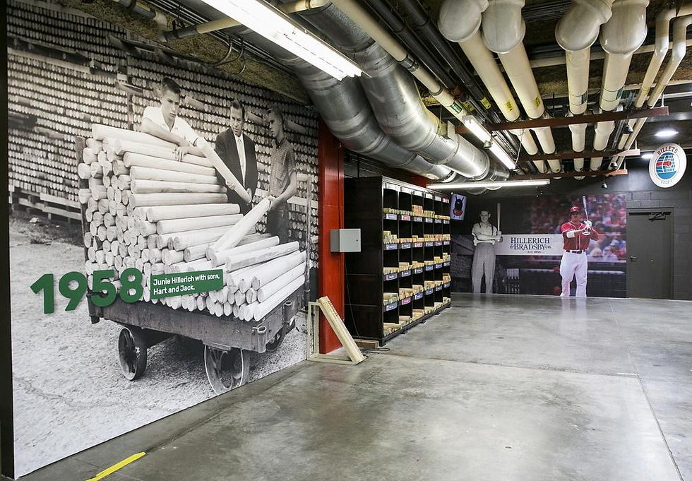 1958 photo of men with baseball bats wall mural, alongside shelves of bats, in an industrial setting with exposed pipes on the ceiling.