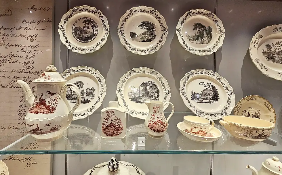 Fine china set with pastoral scenes on display. Includes plates, a teapot, and cups with intricate black and red designs. Vintage script visible.