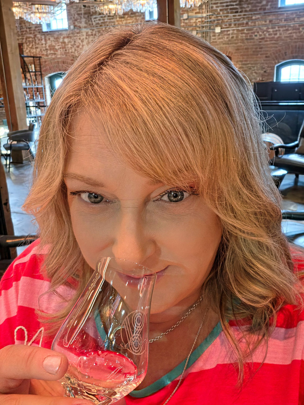 Close-up of a woman tasting gin from a glass in a brick-walled tasting room, wearing a pink striped top at the Spirit of York Distillery in Toronto