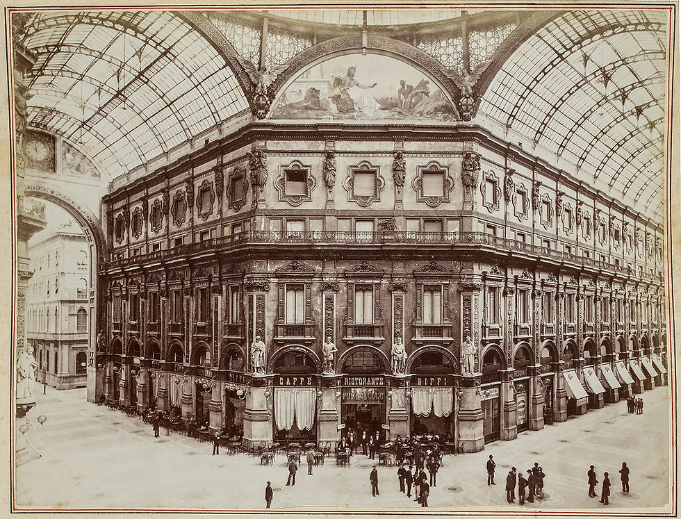 Large indoor gallery with arched glass ceiling, ornate building facade, and groups of people gathered outside "Caffè" and "Ristorante Biffi". This is an old image of the Galleria Vittorio Emanuele II in Milan.