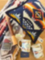 Colorful patterned cushion, mugs, and blanket on wooden floor. Pendleton tags and stickers scattered, creating a cozy, retro vibe.