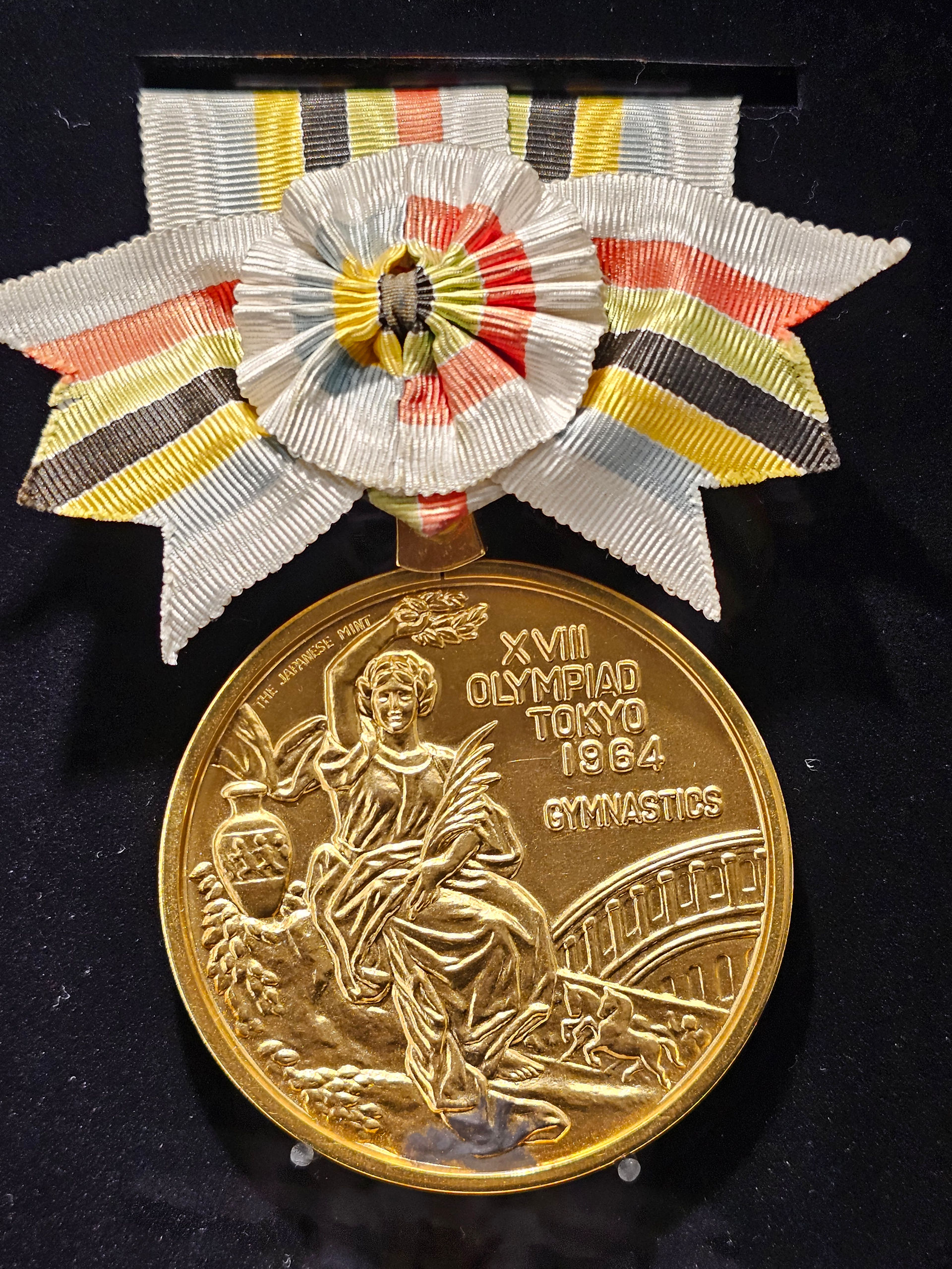 a circular gold disc, an olympic gold medal, inscribed with the games of the XVIII Olympiad tokyo 1964