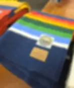 Colorful striped blankets with a Crater Lake Park patch and Pendleton label on a wooden surface, conveying a cozy, rustic vibe. National Park blankets at the store for Pendleton Woolen Mill Tour Washougal.