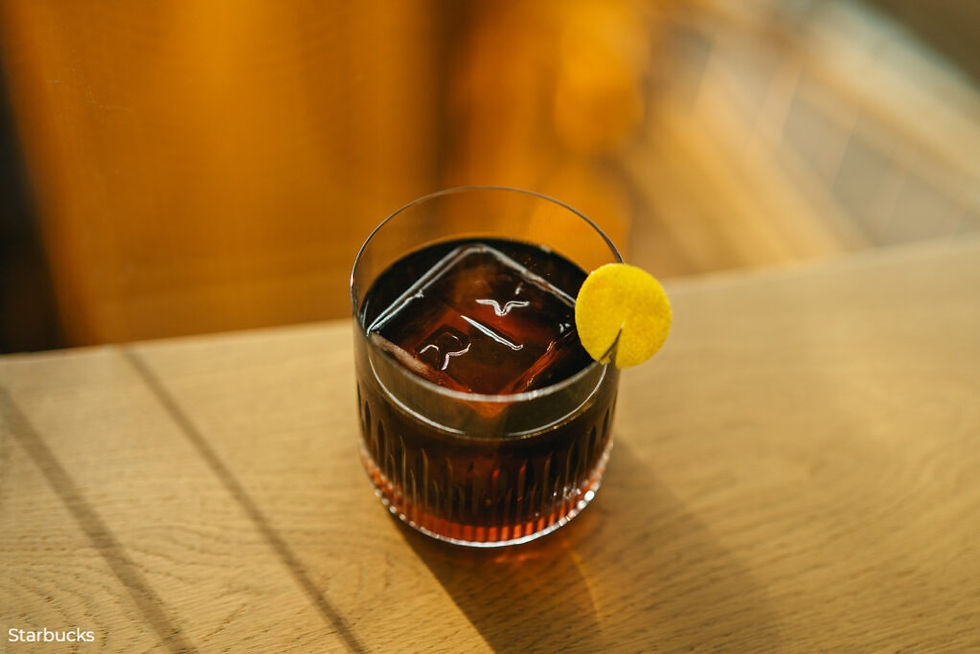 Glass of coffee whisky cocktail with lemon slice on wooden table, warm ambiance. Clear ice cube with letter 'R' visible, relaxed mood.