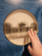 Hand touching a textured, circular model of a historical building on a blue patterned wall in the Silverstone museum. The model is clear, revealing intricate details.