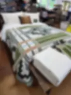 A bed with green and white patterned blanket and pillows in a store display at Pendleton Woolen Mill Tour Washougal. Shelves with more blankets in the background. Cozy setting.