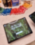 Tablet on a table shows "Are you a fan of fresh rosemary?" with a rosemary background. Colorful wristbands and engraving sign in the background. This sits on a marble topped round table in the foyer of the johnnie walker princes street building.