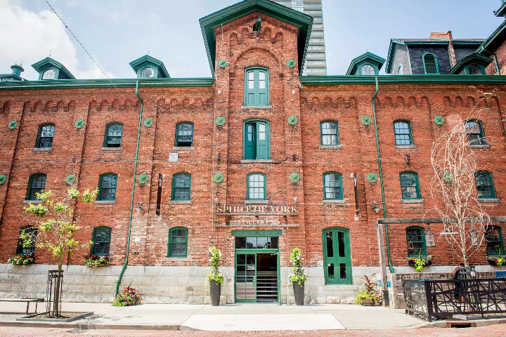 Red brick historic building with green-trimmed windows and doors, sign reading St. Lawrence Market, under a clear sky.