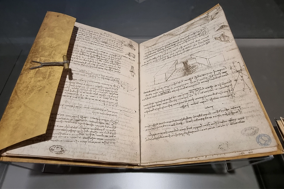 Open notebook with detailed handwritten text and sketches on yellowed pages, displayed under glass in a dimly lit setting.
