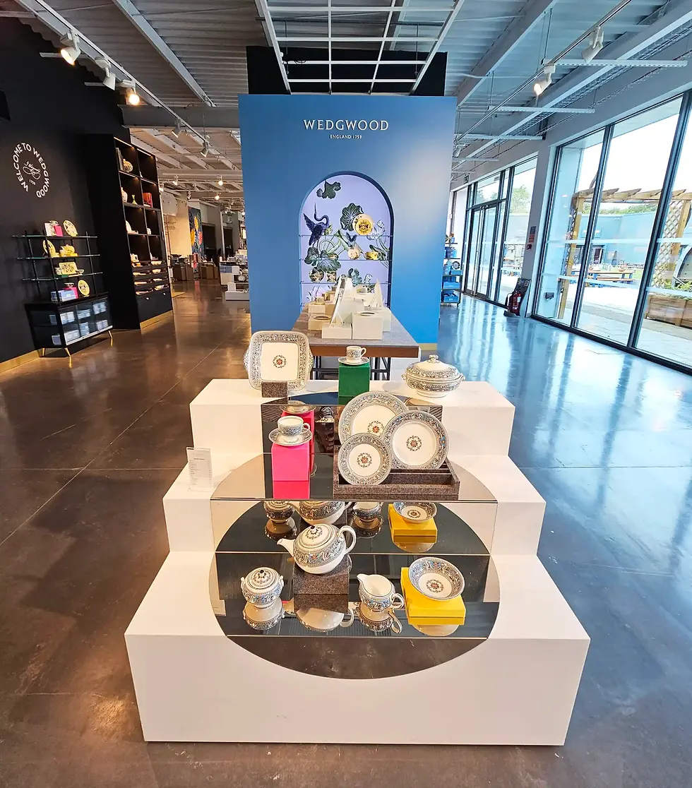 Elegant Wedgwood china display on white stands in a modern showroom. Blue backdrop with floral design. Bright, spacious setting.