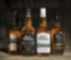 Four Evan Williams bourbon bottles on a rustic wooden surface, set against a dimly lit barrel-filled background.