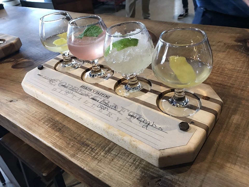4 glasses sit in a tasting tray made from wood. each glass has a different cocktail in it