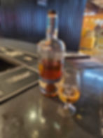 a bottle fo whiskey sits on the stone bar top and a glass of whiskey sits in front of it with teeling written on the glass in white text