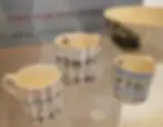 Three alphabet-patterned mugs by Eric Ravilious and a bowl with a steam train design sit on a display at the World of Wedgwood V&A Museum.
