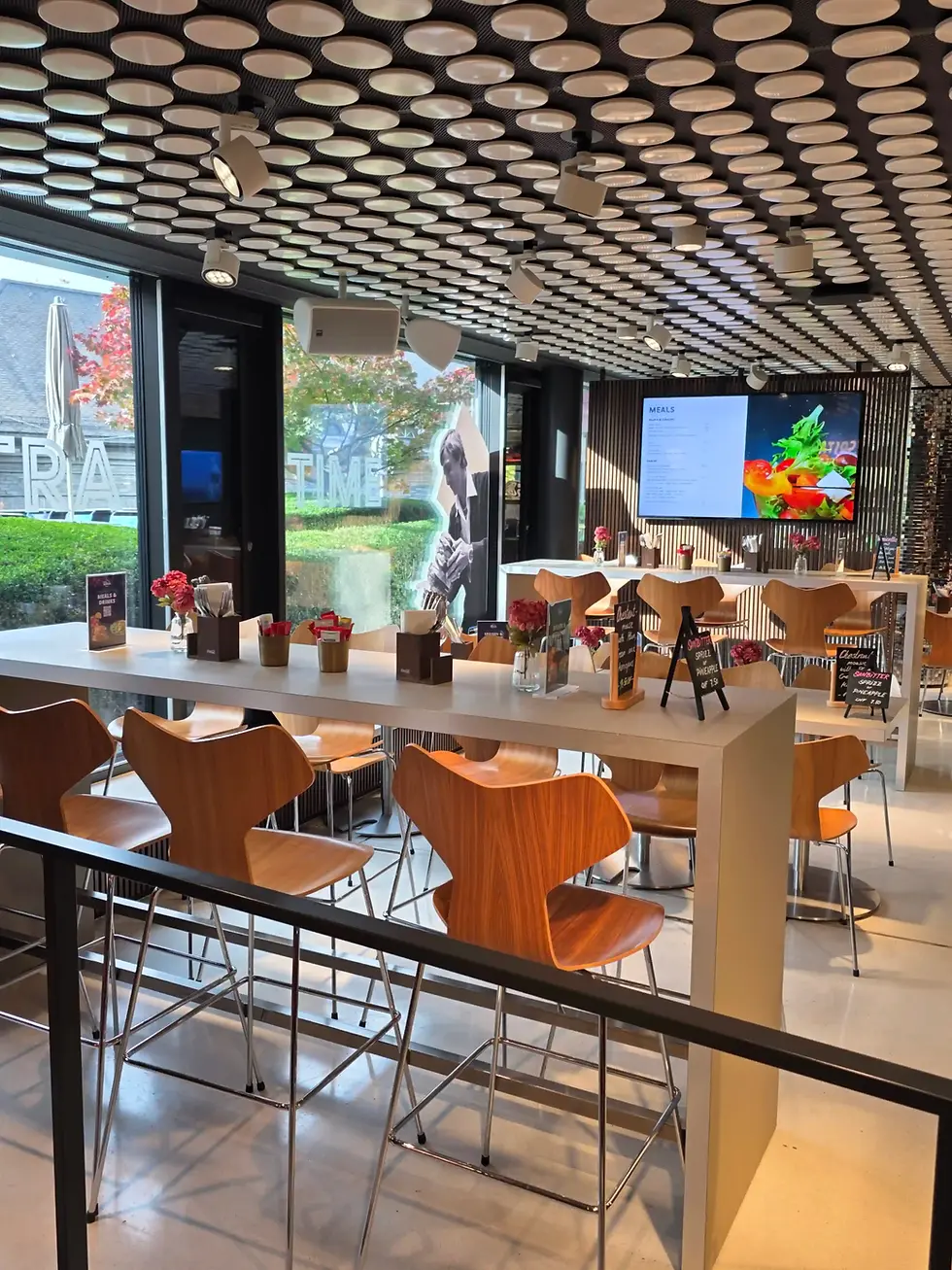 Empty modern café with wood chairs, white tables, patterned ceiling lights, and a digital meal menu by large windows at the FIFA Museum.