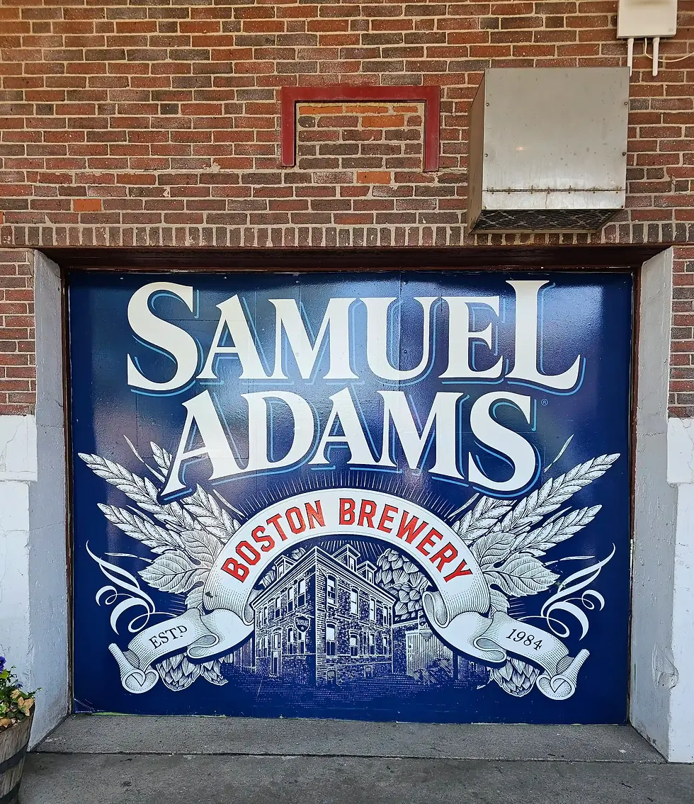 Blue mural on a brick wall reads "Samuel Adams Boston Brewery" with an illustration of a brewery, wheat graphics, and the year 1984.