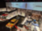 Silverstone Museum exhibit with vintage cars and motorcycles. Brightly colored Hepolite race car in foreground. Historical racing images on walls.