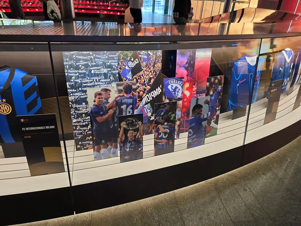 Glass display of soccer club jerseys and posters, including Inter Milan and Chelsea, in a sleek museum-like exhibit at Fifa Museum Zurich.