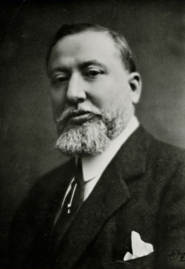 Davide Campari with a beard in a formal suit, pocket square visible. Black and white photo with a serious expression, dark plain background.