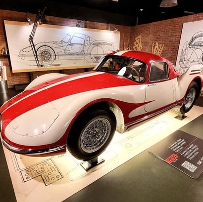 a white sports car with red painted stripes across the bonnet and roof in front of technical drawings at the National Automobile Museum in Turin Italy, the visitor centre and experiences that houses multiple automotive brands