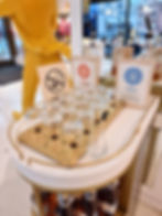 Display of seasonal blends with glass jars and bottles on a gold tray at the johnnie walker princes street visitor experience. "Please do not touch" sign. Bright store interior visible.