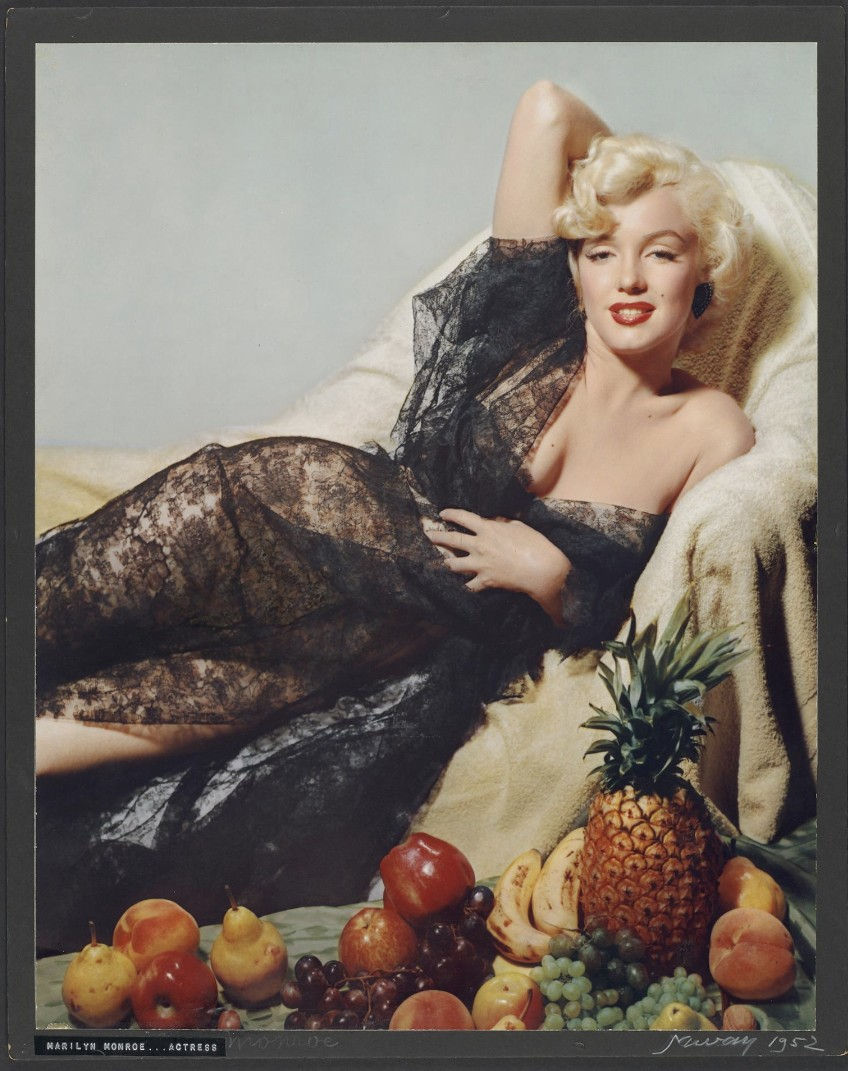 Marilyn Monroe reclines on a cream chaise in a black lace dress, surrounded by fruit; caption reads Marilyn Monroe... actress