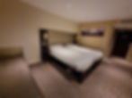 Hotel room with two neatly made twin beds, neutral tones, striped carpet, and floral art on the wall. Cozy and tidy atmosphere.
