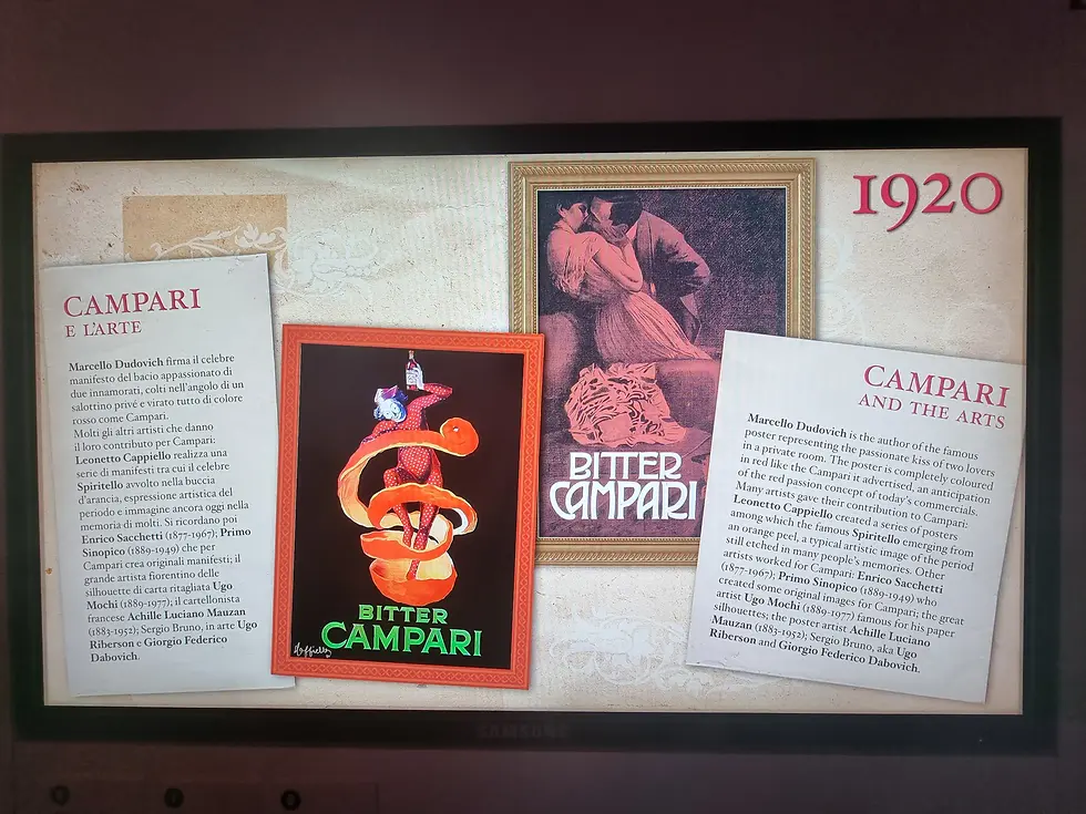 Campari-themed display inside the Galleria Campari, featuring a 1920 poster with lovers, text in Italian and English about art, and a vibrant Bitter Campari ad with an orange spiral.